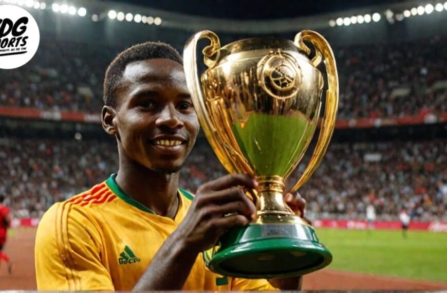 A man in a yellow sports jersey stands in a stadium holding a large golden trophy, celebrating his AFCON victory with the crowd in the background.