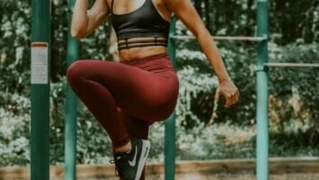 In a serene forest setting, a woman showcases her athletic performance as she gracefully balances on one leg atop outdoor fitness equipment.