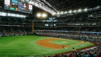 A thrilling MLB game unfolds in a large stadium with a retractable roof, bright lights casting onto the field, as fans eagerly watch from the stands, anticipating every play and decision shaped by MLB rules.