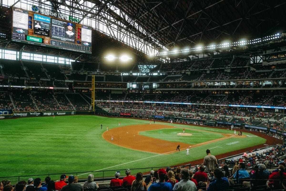 A thrilling MLB game unfolds in a large stadium with a retractable roof, bright lights casting onto the field, as fans eagerly watch from the stands, anticipating every play and decision shaped by MLB rules.