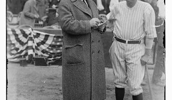 A man in a coat stands next to a baseball player holding a bat at an MLB stadium, capturing the essence of America's pastime.