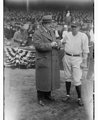 A man in a coat stands next to a baseball player holding a bat at an MLB stadium, capturing the essence of America's pastime.