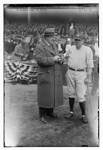 A man in a coat stands next to a baseball player holding a bat at an MLB stadium, capturing the essence of America's pastime.