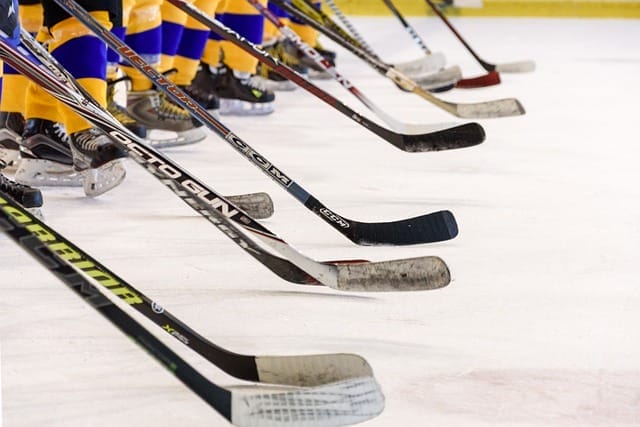 Hockey players in yellow and blue socks, ready for fierce bench battles, line up with their sticks on the ice.