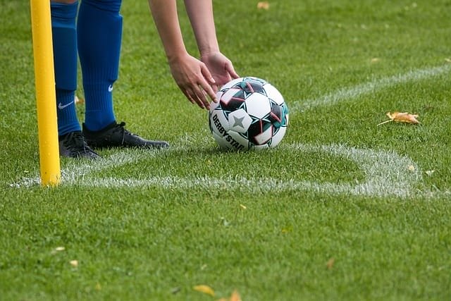 The player, with keen football IQ, carefully sets up the soccer ball for a corner kick on the lush grassy field.