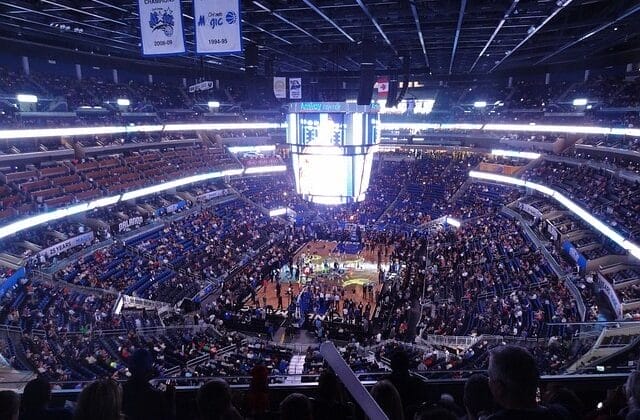 A crowded basketball arena buzzes with excitement as fans watch the NBA game unfold under the bright lights.
