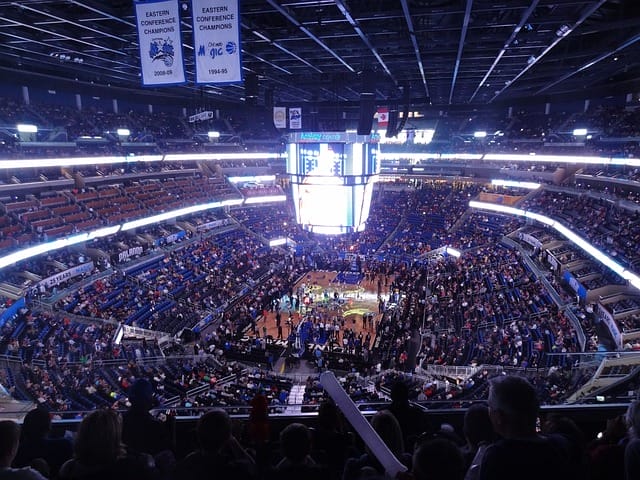 A crowded basketball arena buzzes with excitement as fans watch the NBA game unfold under the bright lights.