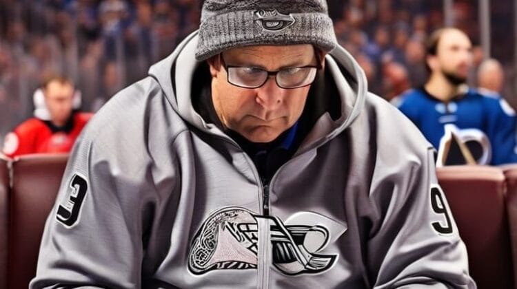 A man wearing glasses, a beanie, and a sports jacket with the number 93 sits in a crowded sports arena, focused on reading a book. This avid NHL fan appears to be enhancing his Hockey IQ even amidst the game's excitement.