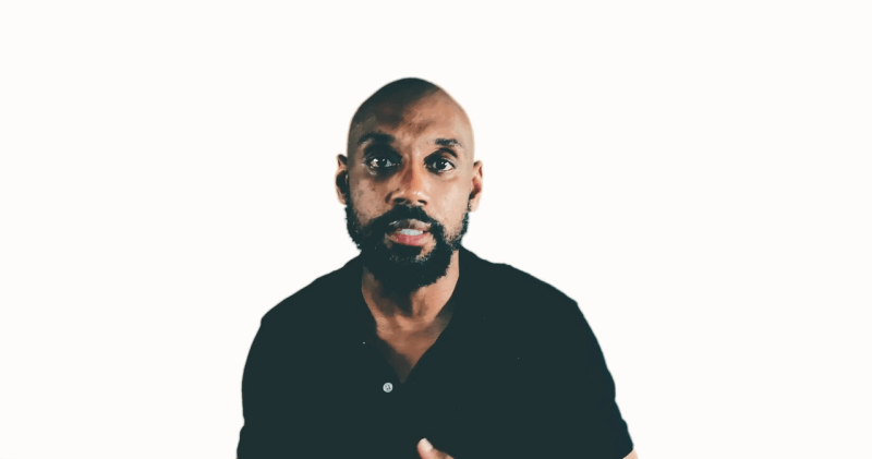 Man with a beard and shaved head, looking more like a football player, wears a black shirt against a plain white background.