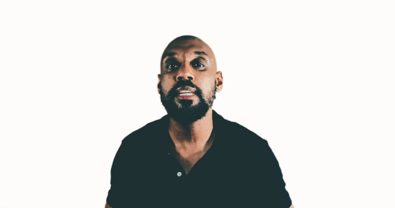 A man with a beard, more like a football enthusiast, wearing a black shirt stands against a white background, looking slightly upward.