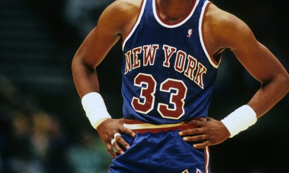 Basketball legend Patrick Ewing, donning his iconic blue New York jersey with the number 33, stands confidently with hands on hips during the intense game.