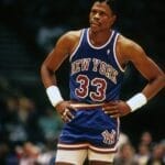 Basketball legend Patrick Ewing, donning his iconic blue New York jersey with the number 33, stands confidently with hands on hips during the intense game.