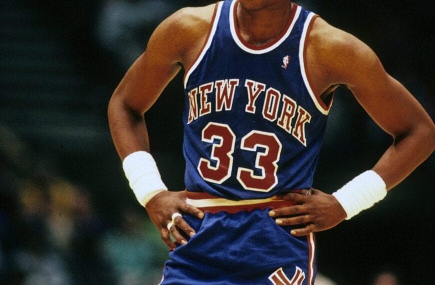 Basketball legend Patrick Ewing, donning his iconic blue New York jersey with the number 33, stands confidently with hands on hips during the intense game.