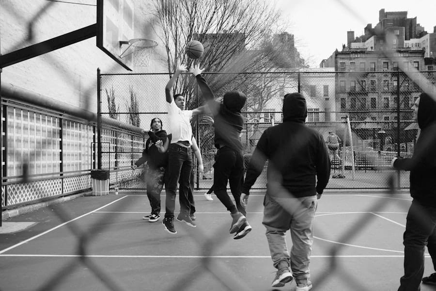 People enjoy a game of basketball on an outdoor court, viewed through a chain-link fence, channeling the spirit and precision of Reggie Miller.