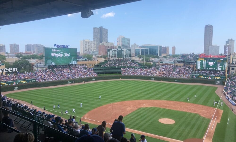 View of a baseball game at a stadium with a city skyline in the background, where fans eagerly discuss an MLB rule change that has added fresh excitement to the season.