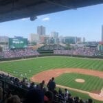 View of a baseball game at a stadium with a city skyline in the background, where fans eagerly discuss an MLB rule change that has added fresh excitement to the season.