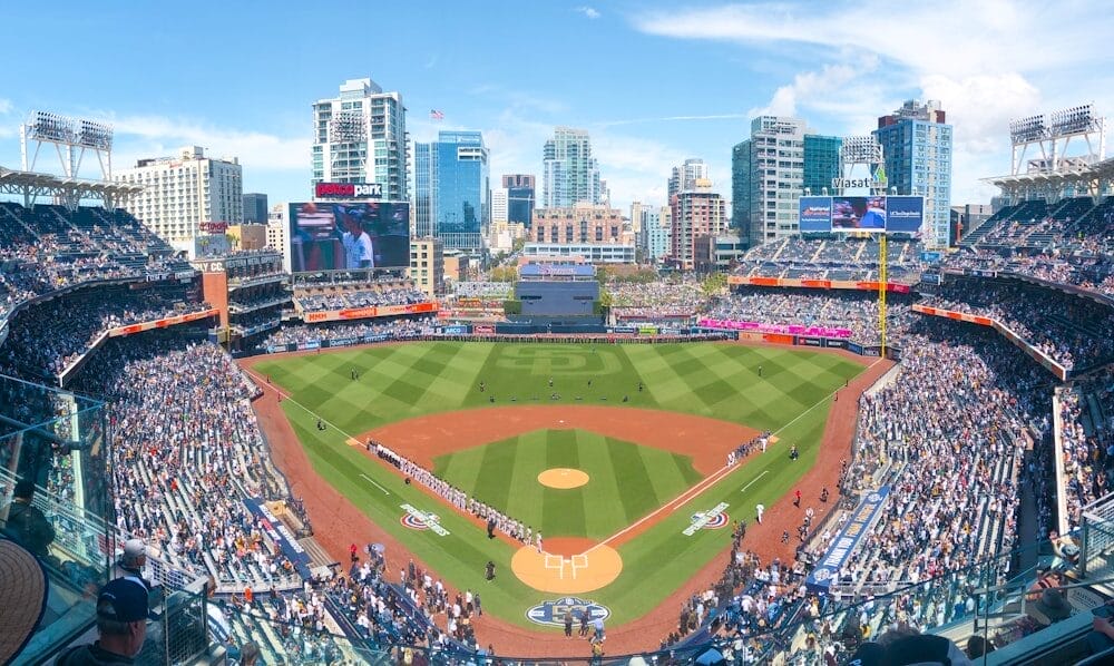 Aerial view of a baseball game at a packed stadium, with the city skyline in the background reflecting the excitement and anticipation as fans discuss the latest MLB rule change.