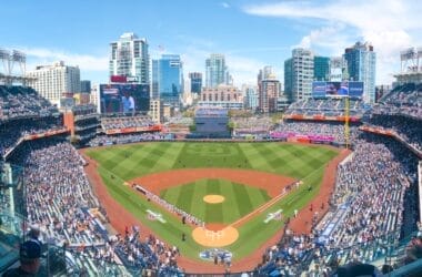 Aerial view of a baseball game at a packed stadium, with the city skyline in the background reflecting the excitement and anticipation as fans discuss the latest MLB rule change.