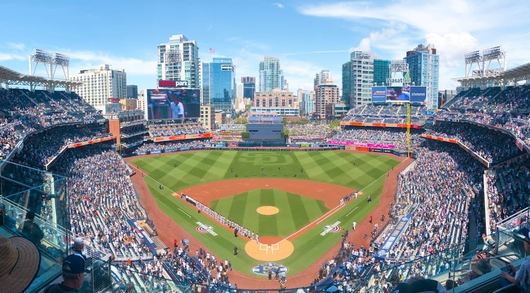 Aerial view of a baseball game at a packed stadium, with the city skyline in the background reflecting the excitement and anticipation as fans discuss the latest MLB rule change.