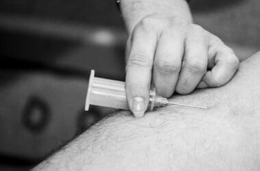 A hand injects a needle into an arm, administering a shot, reminiscent of the precision needed in forecasting NFL injuries. Black and white image.