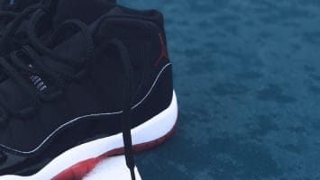 Close-up of a black sneaker with red soles on a wet blue surface, echoing the iconic 90s basketball era and vibrant NBA culture.