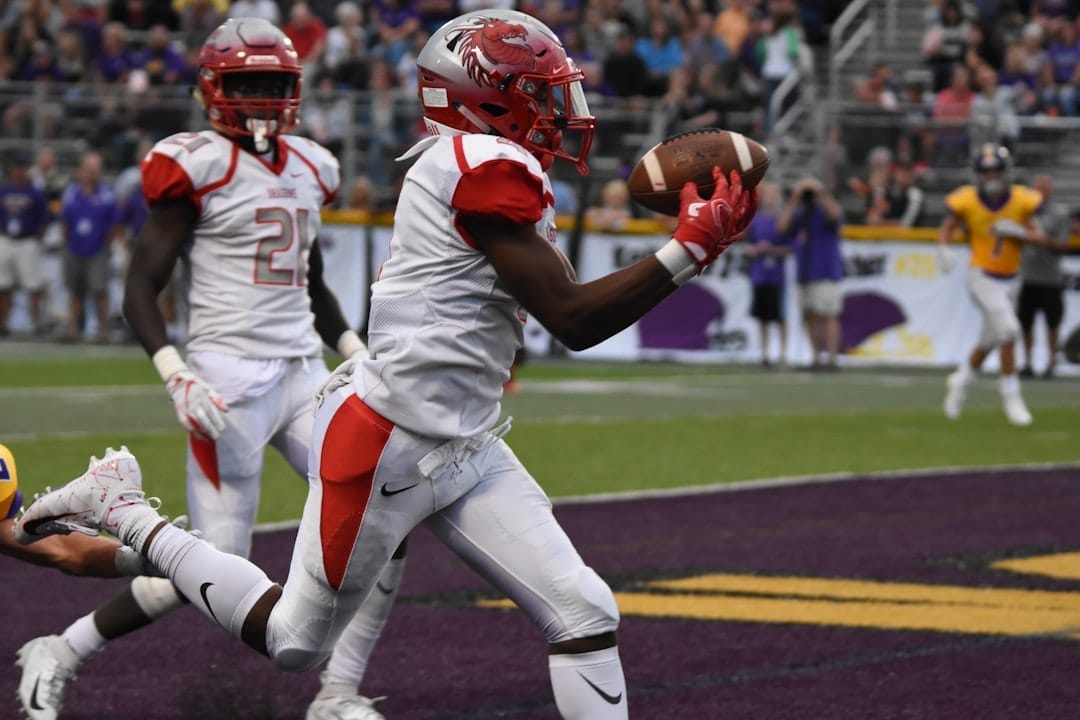 A football player in a white uniform catches a pass in the end zone as machine learning in sports revolutionizes strategies; teammates and the crowd cheer in the background.