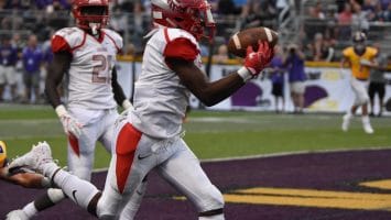 A football player in a white uniform catches a pass in the end zone as machine learning in sports revolutionizes strategies; teammates and the crowd cheer in the background.