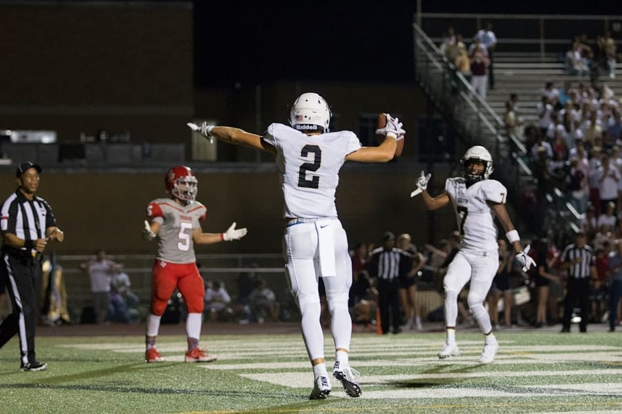 A Canadian football player in white jubilantly celebrates a touchdown as players and a referee look on.