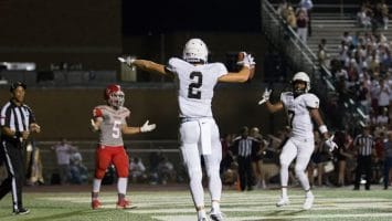 A Canadian football player in white jubilantly celebrates a touchdown as players and a referee look on.
