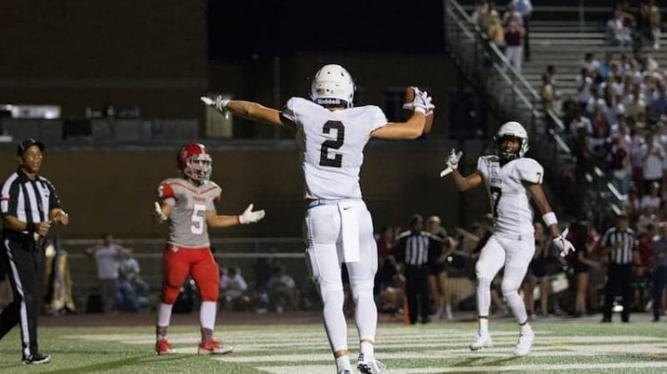 A Canadian football player in white jubilantly celebrates a touchdown as players and a referee look on.
