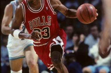 Basketball player in a red jersey skillfully dribbles past his opponent on the court, evoking memories of NBA legends like Scottie Pippen during a game.