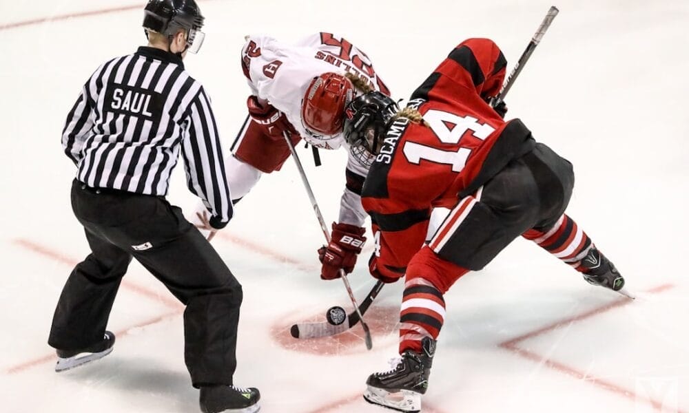 A referee prepares to drop the puck as two ice hockey players, one in a white jersey and the other in a red and black jersey, face off. Poised with their sticks near the ice, they embody the unwritten rules in the NHL, ready to start the play.