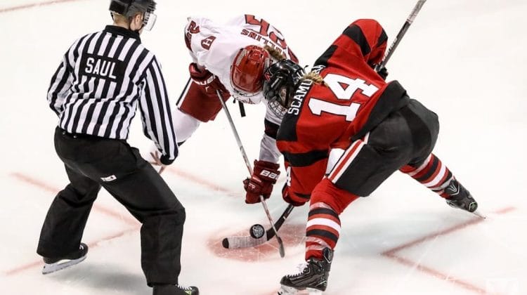A referee prepares to drop the puck as two ice hockey players, one in a white jersey and the other in a red and black jersey, face off. Poised with their sticks near the ice, they embody the unwritten rules in the NHL, ready to start the play.