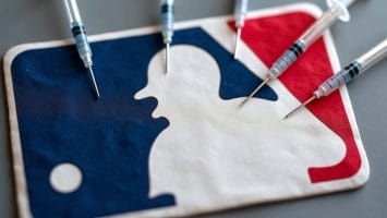 A Major League Baseball logo lies flat, surrounded by six syringes pointing toward it. This image symbolizes the deep connection to MLB controversies, reflecting hot-button issues in the sport. The syringes are evenly spaced around the iconic batter silhouette and baseball emblem.