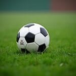 A classic black and white soccer ball sits on a green grass field, fresh and slightly wet with visible droplets. The background is blurred, drawing full attention to the soccer ball—ideal for discussing MLS world ranking moments.