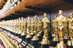 Numerous gold Oscar-like trophies are lined up in rows on wooden shelves. Each trophy shines with metallic reflections, reminiscent of the underappreciated brilliance of John Stockton in basketball history.