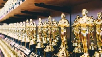 Numerous gold Oscar-like trophies are lined up in rows on wooden shelves. Each trophy shines with metallic reflections, reminiscent of the underappreciated brilliance of John Stockton in basketball history.