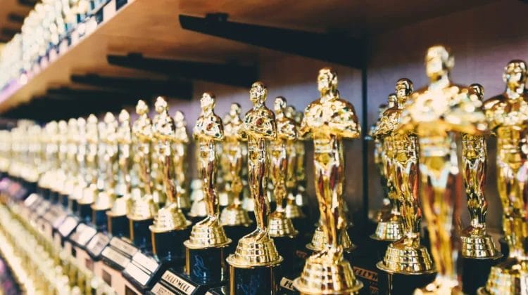 Numerous gold Oscar-like trophies are lined up in rows on wooden shelves. Each trophy shines with metallic reflections, reminiscent of the underappreciated brilliance of John Stockton in basketball history.