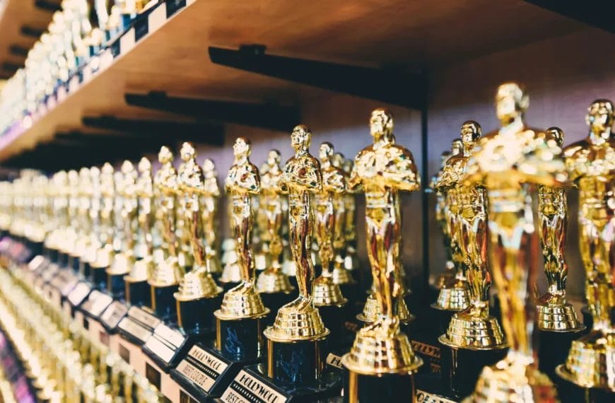Numerous gold Oscar-like trophies are lined up in rows on wooden shelves. Each trophy shines with metallic reflections, reminiscent of the underappreciated brilliance of John Stockton in basketball history.