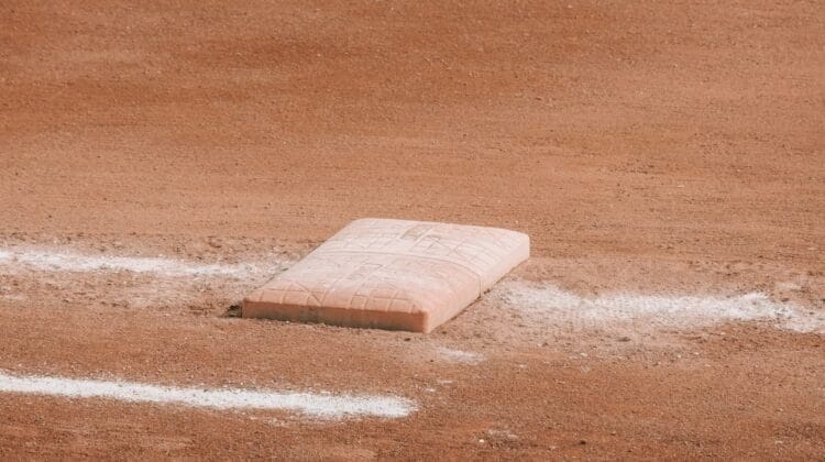 A close-up of a single base on a baseball field sits on smooth, reddish-brown dirt. White chalk lines border the worn base, recalling Baseball Rules During the Dead Ball Era as sunlight casts soft shadows, highlighting the field’s classic texture.