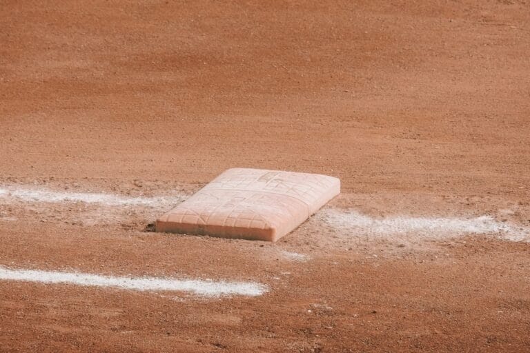 A close-up of a single base on a baseball field sits on smooth, reddish-brown dirt. White chalk lines border the worn base, recalling Baseball Rules During the Dead Ball Era as sunlight casts soft shadows, highlighting the field’s classic texture.