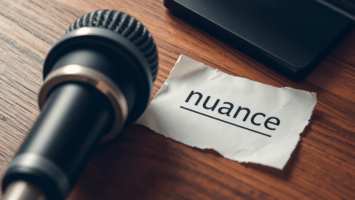 A black microphone rests on a wooden table beside a torn piece of white paper with "nuance" underlined, highlighting the subtlety often missing from sports debate shows in traditional sports media that sometimes misinform fans.