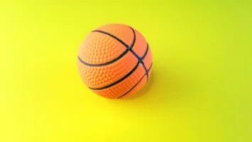 A small, textured orange basketball with black lines is centered on a bright yellow background. Perfect for anyone learning how to argue sports effectively, this vibrant and minimalistic image captures the spirit of spirited debate.