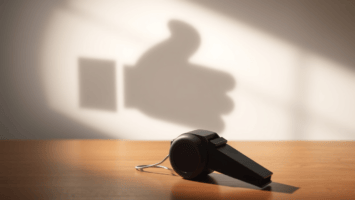 A black whistle rests on a wooden surface. On the wall behind it, light casts the whistle’s shadow as a “thumbs up,” suggesting approval or positivity—much like a social media like, in this warmly lit, encouraging scene.